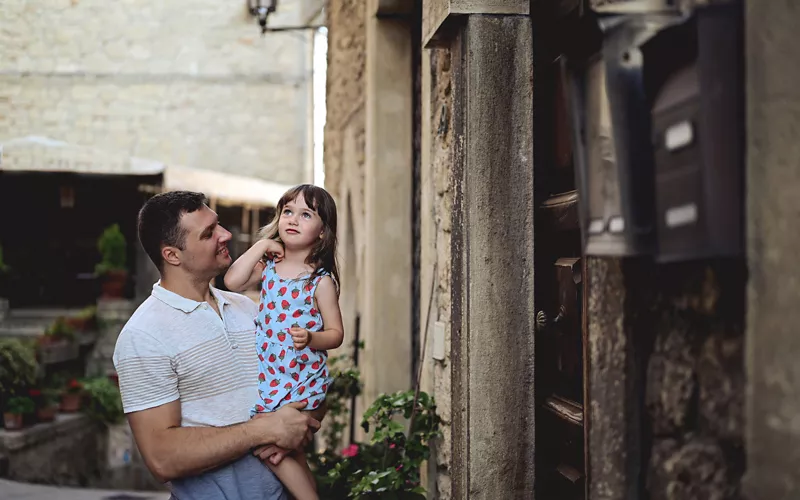 Un padre con in braccio una bambina in un borgo