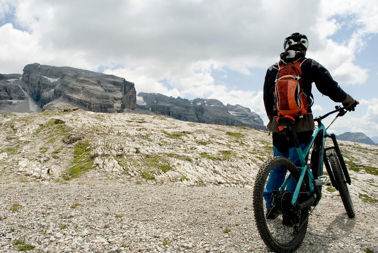 man with an electric bike, e-bike, ebike, mtb, observes Grosté Peak, Dolomite mountains, Madonna di Campiglio, summer, sport, adventure, travel, Alps, Trentino, Alto Adige, Italy