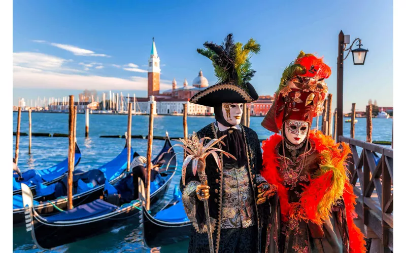 A man and a woman wearing traditional costumes of the Venice Carnival with the Island of San Giorgio Maggiore in the background