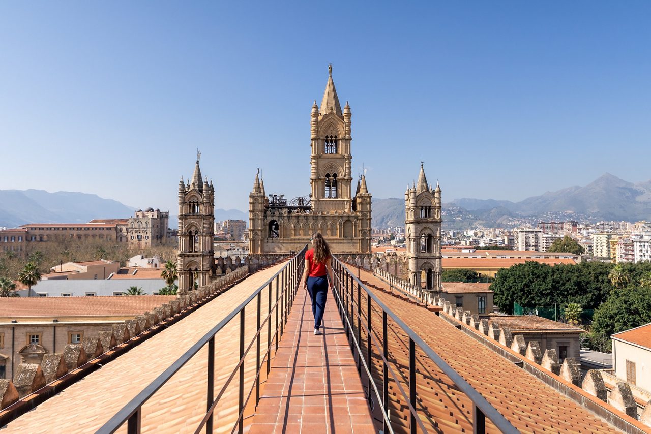 Woman tourist visitor walking on the rooftop catwalk of the Palermo Cathedral or Cattedrale di Palermo with bell towers in the background on a nice sunny afternoon in Palermo, Sicily, southern Italy.