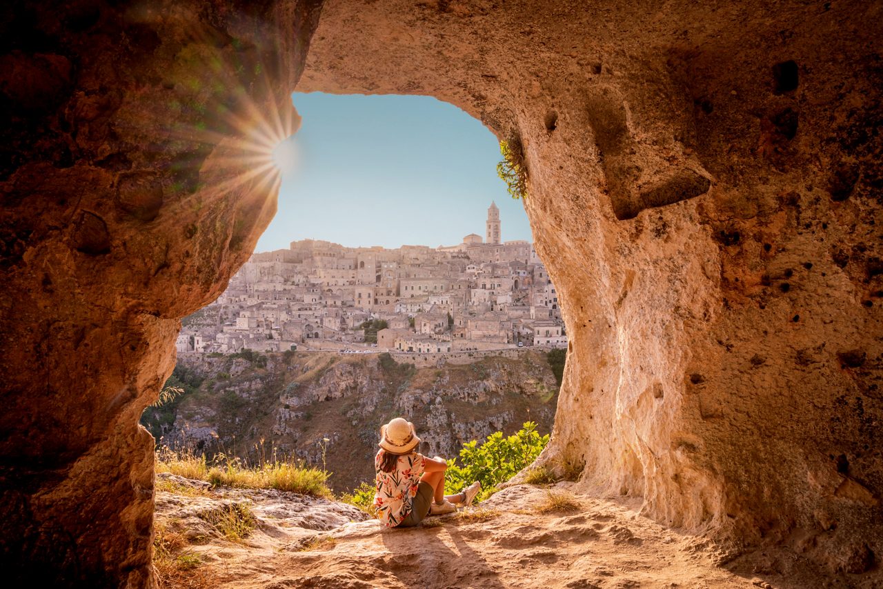 Tourist woman admiring Matera from a cave at sunset, Basilicata, Italy. Sunburst. European Capital of Culture 2019