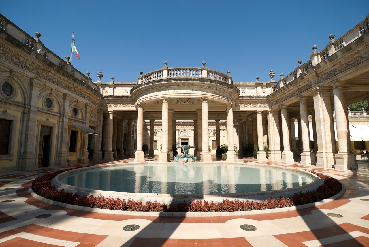 Archway with marble colonnade and a reflecting pool at a thermal spa building in Montecatini Terme. The building is in a 18th century style and has ornate decoration.