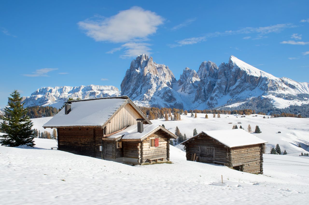Wooden mountain chalets with a view on the Langkofel and Plattkofel (Sassolungo and Sassopiatto) dolomites mountains at the Alpe di Siusi or Seiser Alm in South Tyrol, Italy in winter.
