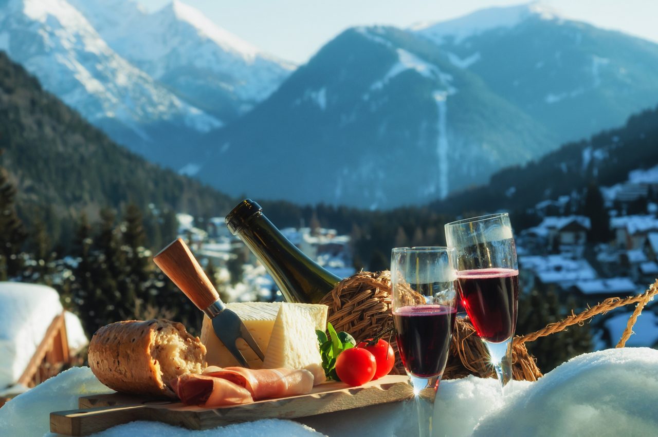 Traditional Italian food outdoor in sunny winter day. Romantic alpine picnic in Madonna Di Campiglio with mountains background, North Italy.