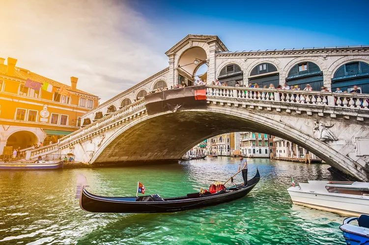 Vista di una gondola sul Canal Grande con Ponte di Rialto al tramonto.