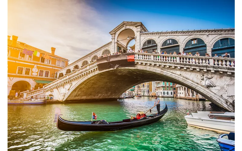 Vista di una gondola sul Canal Grande con Ponte di Rialto al tramonto.