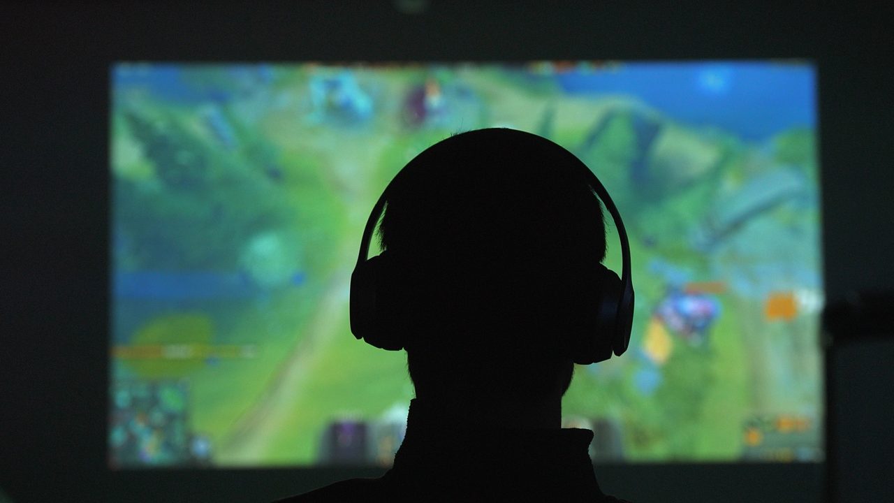 Back view of silhouette of a young man plays video games in dark room watches a movie in headphones