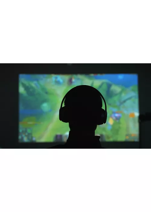 Silhouette di spalle di un uomo con delle cuffie che gioca con un videogame davanti a un grande schermo in una stanza scura