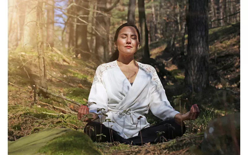 Donna che pratica meditazione nella foresta baciata dai raggi del sole.