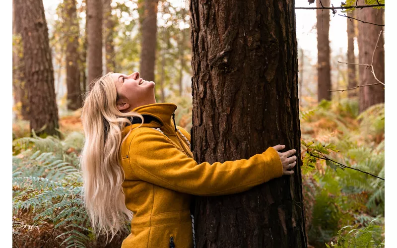Ragazza che abbraccia un albero secolare per la pratica del tree hugging.