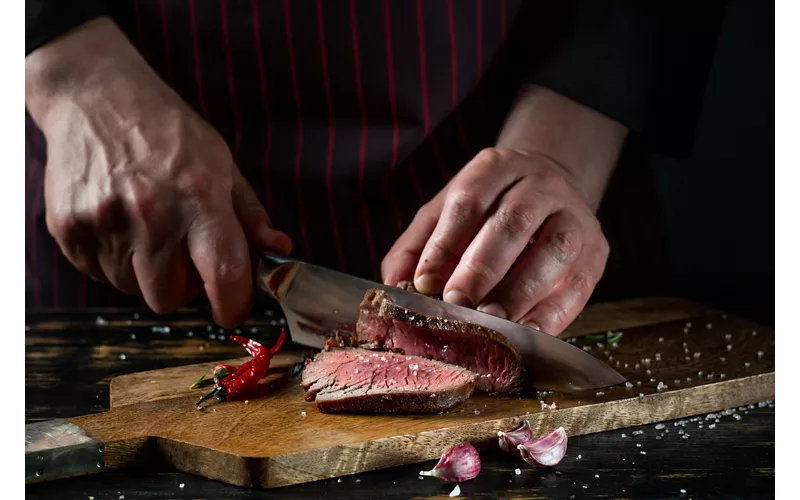 Close-up of a chef's hands cutting a porterhouse steak.