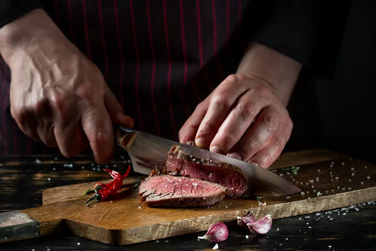 Close-up of a chef's hands cutting a porterhouse steak.