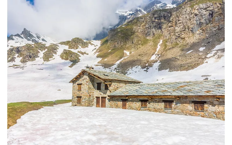 Esterno di uno dei rifugi del Parco su un pianoro innevato, con le montagne sullo sfondo