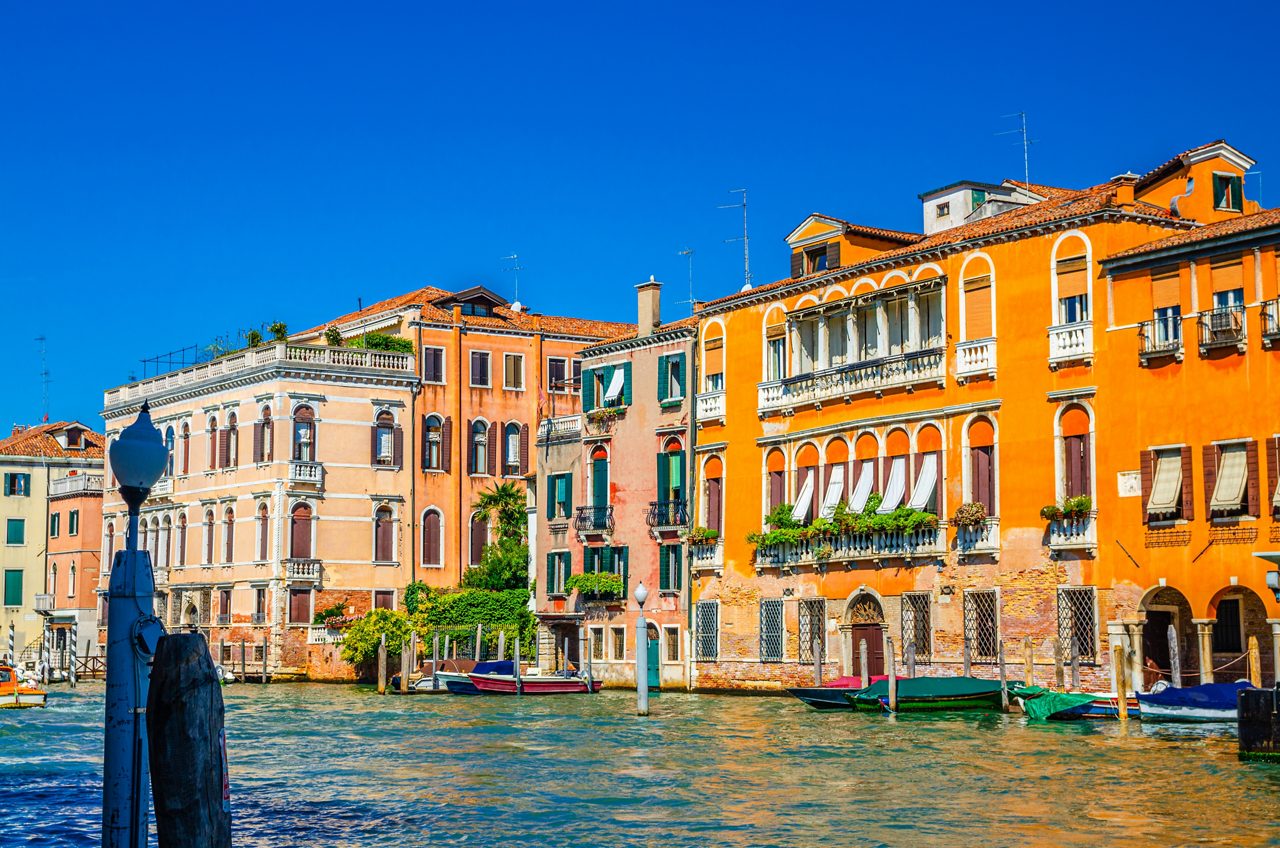 Grand Canal waterway with colorful multicolored palace buildings and moored boats in Cannaregio sestiere Venice historical city centre, blue clear sky background in summer day, Veneto Region, Italy