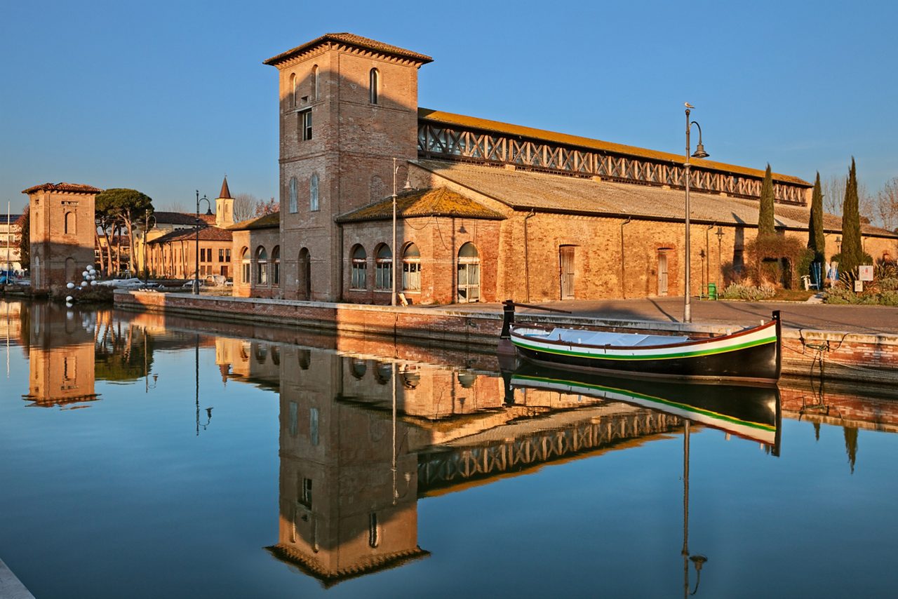 Cervia, Ravenna, Emilia Romagna, Italy: the port canal with the ancient salt warehouse and an historic fishing boat of the Adriatic sea 