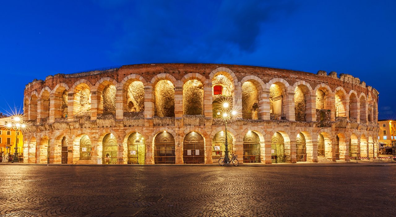 Ancient amphitheater arena di verona in italy like coliseum with nighttime illumination and evening blue sky